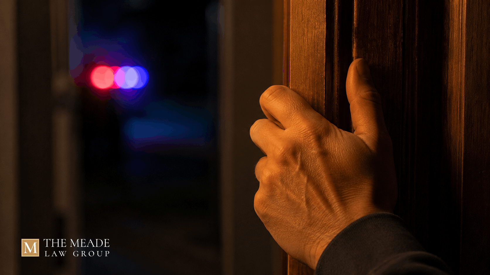 Hand gripping a front door frame at night with warm indoor light and red and blue emergency lights glowing in the background, symbolizing contributing to the delinquency of a minor charge in Ohio.
