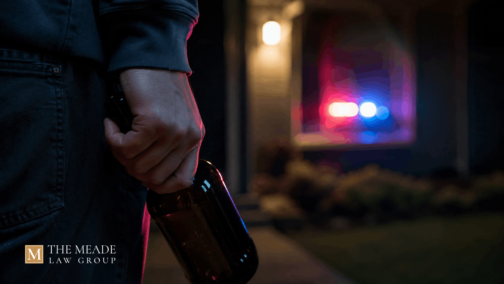 Hand holding bottle behind back with police lights in background, symbolizing an underage drinking charge in Ohio