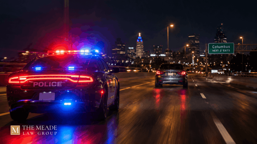 Police cruiser with flashing lights pursuing a car at night on an Ohio road, illustrating a failure to comply charge.